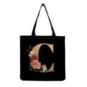 Black canvas tote bag detail featuring elegant gold letter C and vintage floral print design.