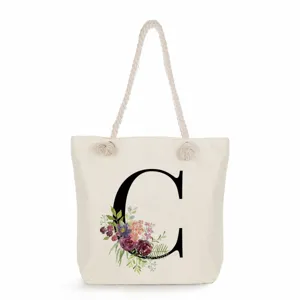 Nahaufnahme der Segeltuchtasche mit floralem Buchstaben-Druck und stabilen Kordelgriffen.