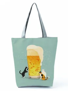 Vue détaillée du charmant imprimé graphique de bière et chats sur le sac cabas vert.