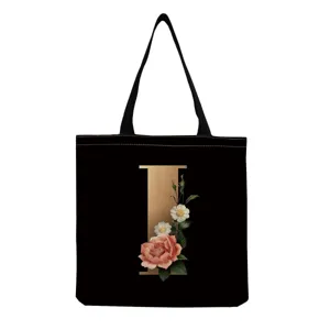 Detail view of black canvas tote bag featuring gold letter I and vintage floral print design.