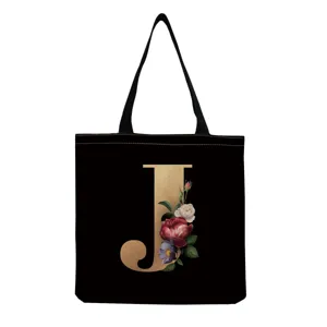 Black canvas tote bag detail featuring a gold floral monogram letter J design closeup.
