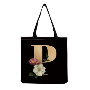 Close-up of black canvas tote bag with gold letter P and vintage floral print detail.