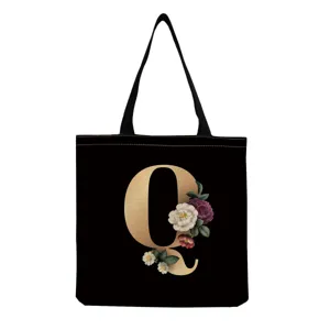 Black canvas tote bag featuring a vintage gold letter Q and elegant floral print for daily use.