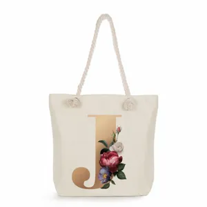 Close-up detail of canvas tote bag featuring a golden letter J and floral print design.
