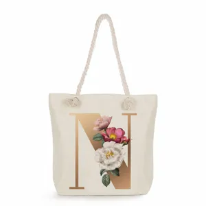 Close-up detail of the canvas tote bag featuring a large golden initial N and floral print.