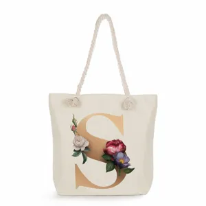 Detailed view of a beige canvas tote bag featuring a gold letter S and elegant floral print.