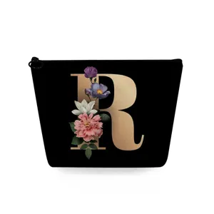 Zwarte cosmetische tas detail met gouden monogram letter R en vintage bloemenprint.