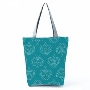 Close-up detail of the teal tote bag featuring a unique white geometric eye pattern design.