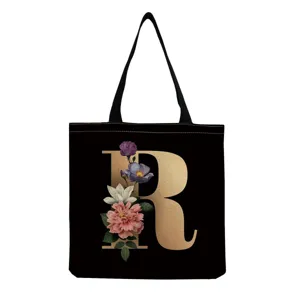 Black canvas tote bag with gold letter R and vintage floral print for daily shopping use.