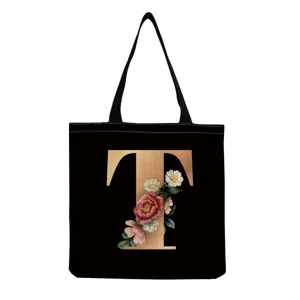 Detailed close-up of the black tote bag featuring a golden letter T and vintage floral.