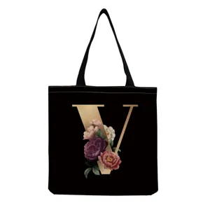 Close-up of black canvas tote bag featuring elegant gold letter V and vintage floral graphic.