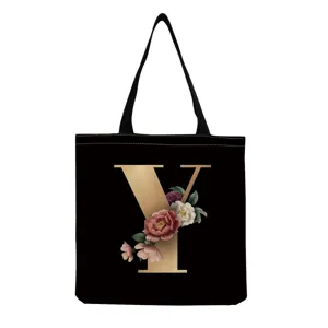 Black canvas tote bag with gold letter Y and floral print, casual shoulder handbag.