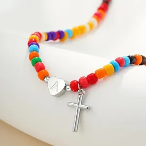 Prachtig detail van kleurrijke kralenketting met zilveren kruis en letter hart hangertje.