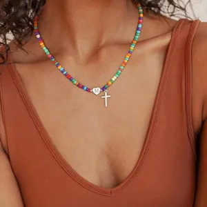 Detailopname van de kleurrijke kralenketting met een kruis hangertje en een hart charm.