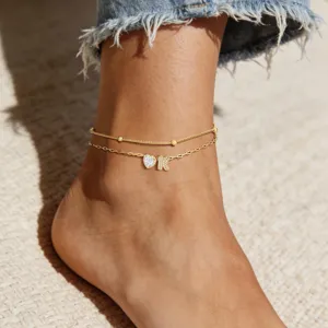 Gros plan détaillé d'un bracelet de cheville doré double chaîne avec cœur en zircon et lettre K.