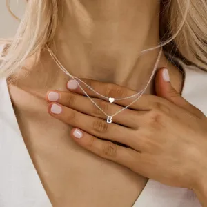 Gros plan détaillé du collier double couche avec pendentifs cœur et lettre B au cou.