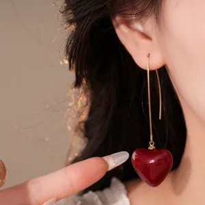 Vue détaillée de élégantes boucles d'oreilles pendantes dorées avec pendentif cœur rouge.