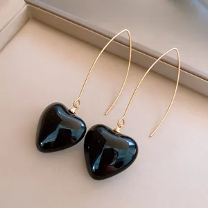 Élégantes boucles d'oreilles pendantes dorées avec pendentifs cœur noirs lisses.