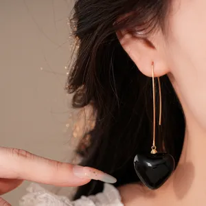 Detail des boucles d'oreilles pendantes d'or avec un pendentif coeur noir brillant.
