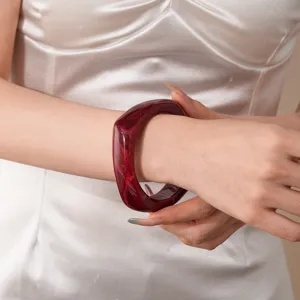 Detailed close-up shot of a dark red geometric resin acrylic bangle bracelet worn on wrist.