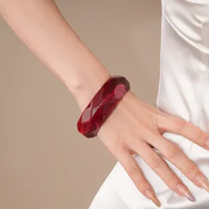 Detailed shot of a dark red faceted acrylic bangle bracelet worn on wrist, close-up texture.