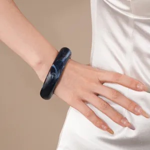 Close-up detail of dark blue marbled resin chunky bangle bracelet worn on model wrist.
