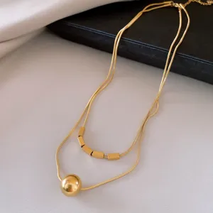Détail d'un collier minimaliste doré à double rang en acier inoxydable aux pendentifs géométriques.