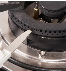 Close-up of serrated cleaning tool unclogging gas stove burner holes effectively