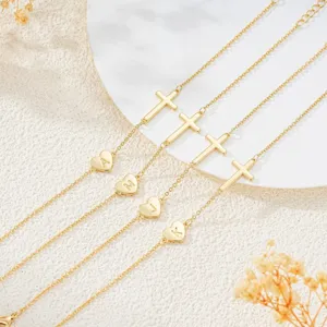 Detailed close-up of gold-plated cross and letter heart charm bracelet, elegant fashion style.