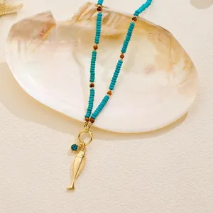 Detalle de un collar de estilo marino con cuentas turquesas y un colgante de pez dorado.