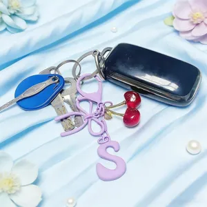 Cute cherry keychain detail shot featuring a stylish bow charm and car key fob on blue silk.