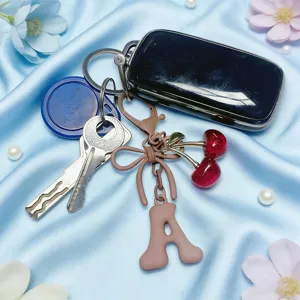 Detailed close-up of cute cherry pendant keychain with letter A charm on blue silk background.