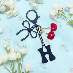 Close-up of cute cherry pendant keychain with blue bow and letter charm for stylish bag decor.