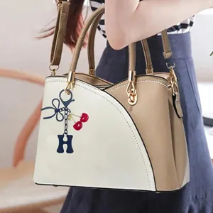 Elegant two-tone women handbag with cute cherry and letter pendant for daily fashion use.