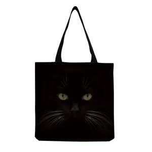 Black canvas tote bag detail featuring a realistic dark cat face print with glowing eyes.