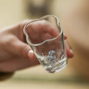 Transparent glass tea cup featuring an irregular wavy rim and elegant crane pattern design.