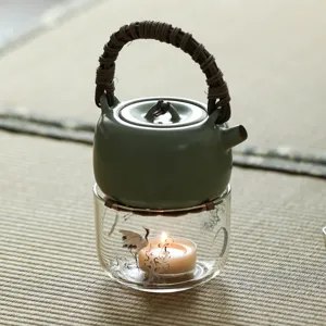 Théière en céramique céladon avec chauffe-thé en verre et bougie, fond de tatami rustique.