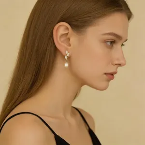 Close-up detail of elegant gold alloy leaf and pearl drop earrings worn by fashion model.