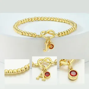 Bracelet de perles en or avec charm nœud de cœur, initiale personnalisée et pierre de naissance.