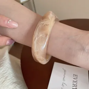 Detalle de brazalete de resina irregular beige, accesorio de pulsera vintage elegante.