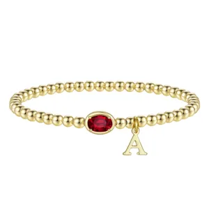 Bracciale di perle dorate con pietra rossa ovale e ciondolo con lettera A da donna.