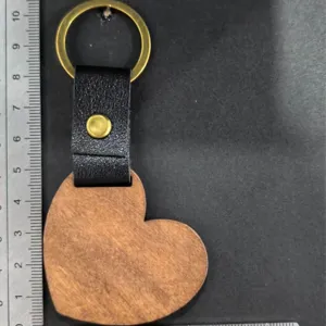 Detailopname van een houten hart sleutelhanger met zwarte lederen band en gouden ring.