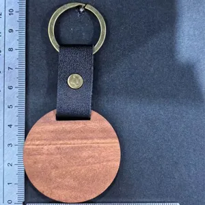 Runder Holzschlüsselanhänger mit schwarzem Lederriemen und Metallring, praktisches Design.