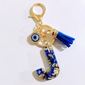 Gros plan détaillé du porte-clés en résine lettre J bleue avec pompon et amulette mauvais œil.