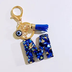 Detailed view of the blue letter M keychain with evil eye charm, tassel, and gold clasp.
