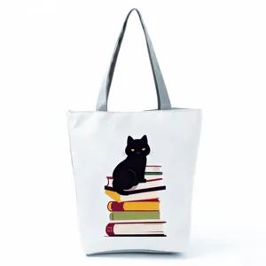 Detail view of the white canvas tote bag featuring a cute black cat and books print.