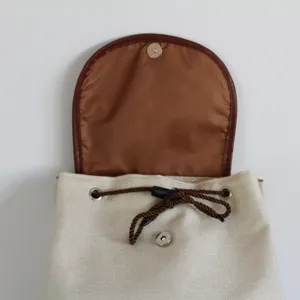 Canvas drawstring backpack detail, beige fabric with brown leather flap and secure snap closure.