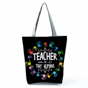 Detailed view of the black canvas tote bag featuring colorful handprints and teacher theme text.