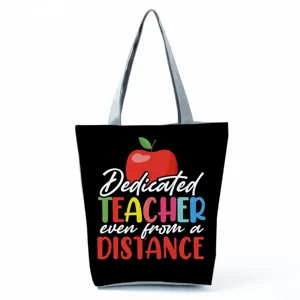 Detailed view of the black canvas tote bag featuring teacher theme apple graphic and text.