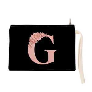 Detailed view of black cosmetic pouch with pink floral letter G, white wrist strap and zipper.